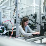 A female engineer focuses on her laptop amidst advanced tech equipment in a lab.
